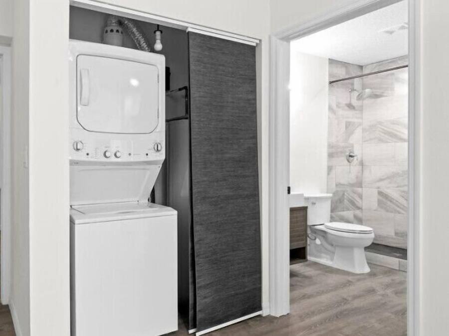 A modern bathroom with a built-in washer and dryer, a glass shower enclosure, and a toilet.