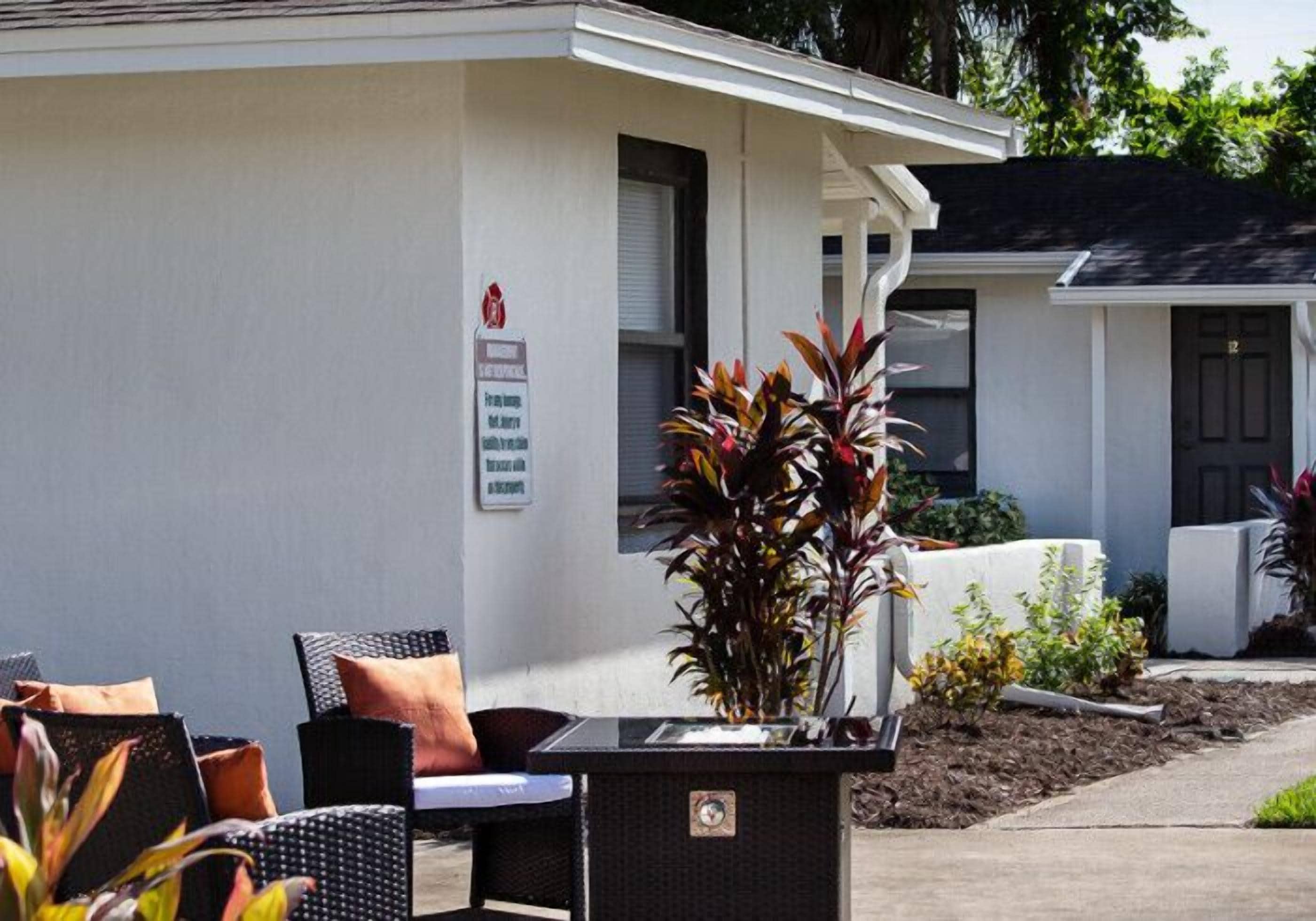 A building with a white exterior, a sign on the wall, outdoor furniture, and plants.