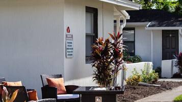A building with a white exterior, a sign on the wall, outdoor furniture, and plants.