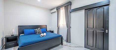 Un dormitorio con cama, mesitas de noche, ventilador de techo, aire acondicionado y armario.