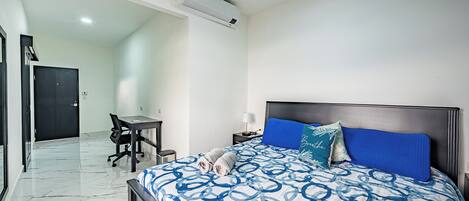 A bedroom with a bed, a desk, and a chair, an air conditioning unit, and a door.