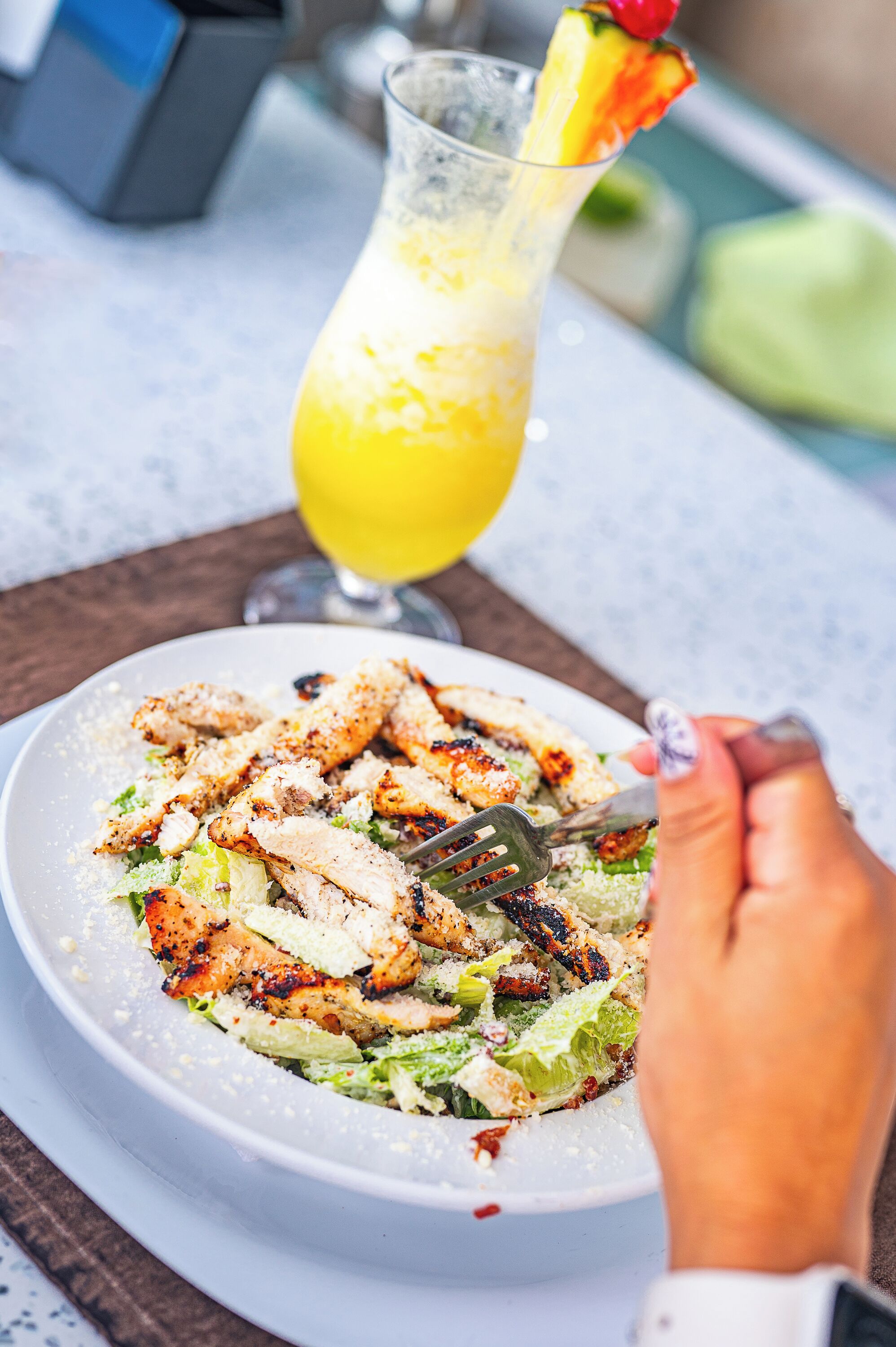A plate of grilled chicken salad with a glass of orange juice in the background.