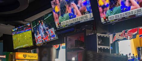 A bar area with multiple screens displaying sports events, a shelf with bottles, and a sign reading "Imperial".