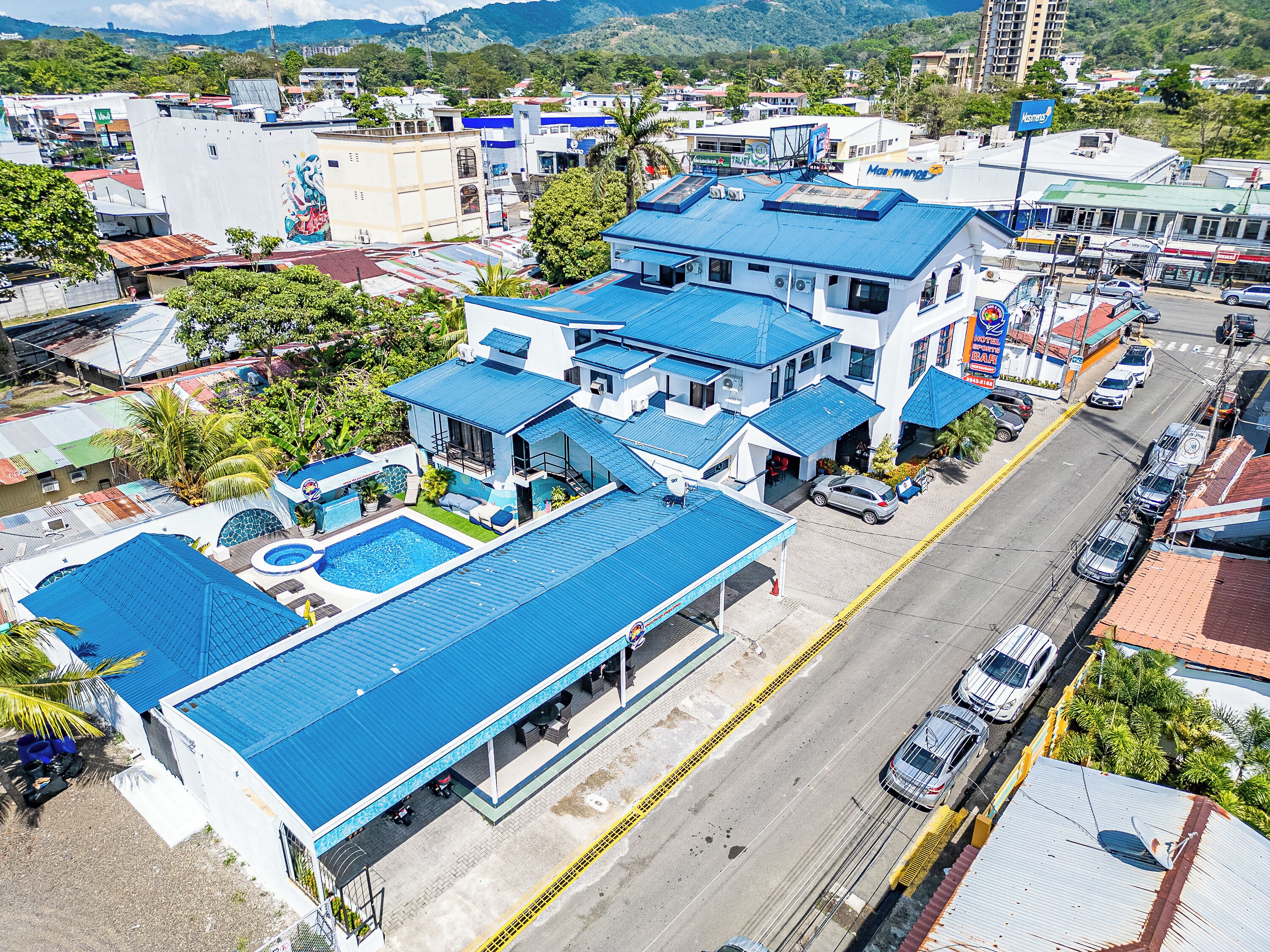 A hotel with a swimming pool, multiple blue-roofed buildings, and a street view.