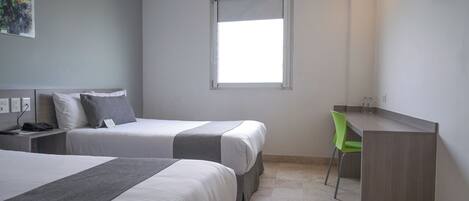 A hotel room with two beds, a desk, a chair, and a window.