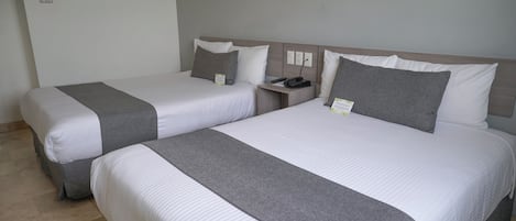 Dos camas individuales con ropa de cama gris y blanca, una mesita de noche con un teléfono y un aplique de pared.