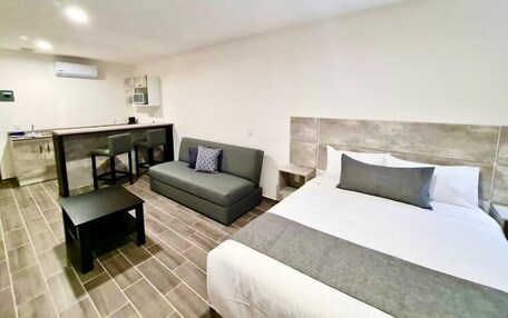 A hotel room with a bed, a sofa, a small table, a kitchenette, and a microwave.