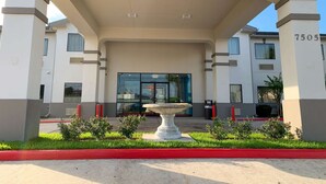A modern building entrance with a covered walkway, a central fountain, and a number '7505' on the right pillar. - Motel 6 Houston, TX - Hwy 249 and Fallbrook (Houston)