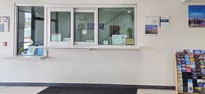 A hotel reception area with a check-out time sign, a window with a view of the interior, and a display of travel books.