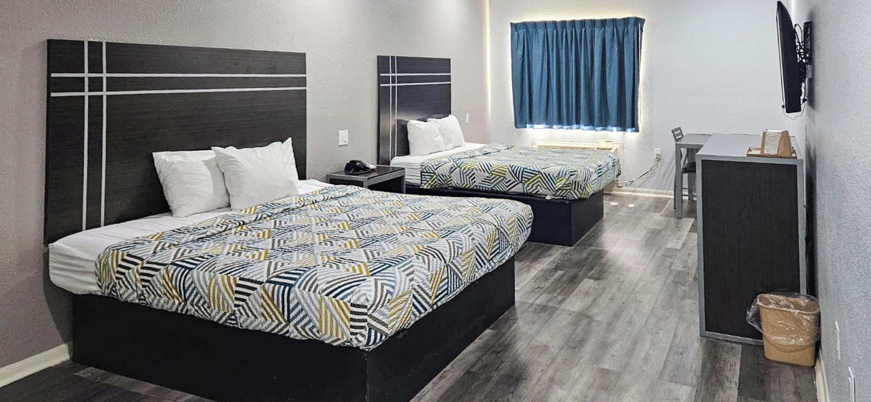 Una habitación de hotel con dos camas, un escritorio y una ventana con cortinas.