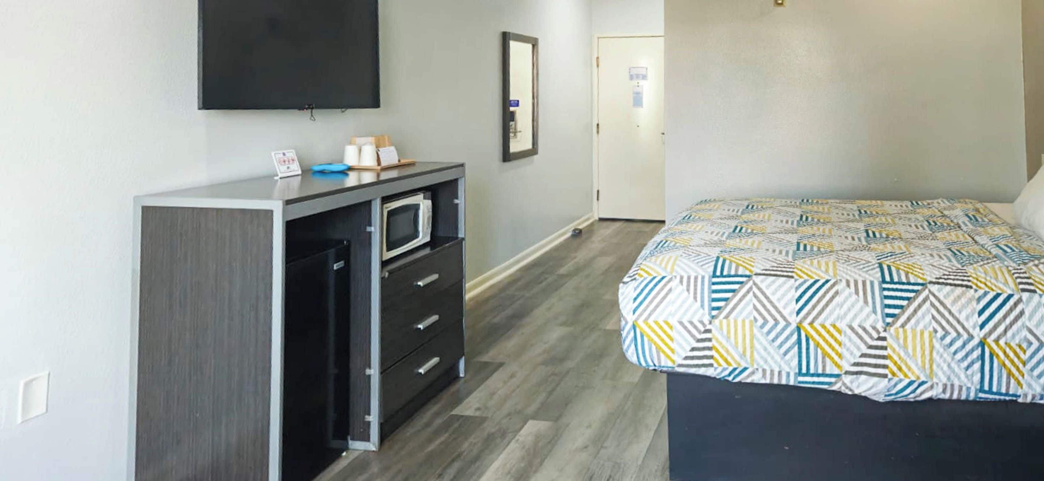 A hotel room with a bed, a desk with a microwave, a television, and a door.