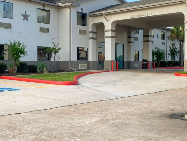 A building with a covered entrance labeled "Clearance 14," a parking lot with marked handicapped spaces, and a small tree-lined area.