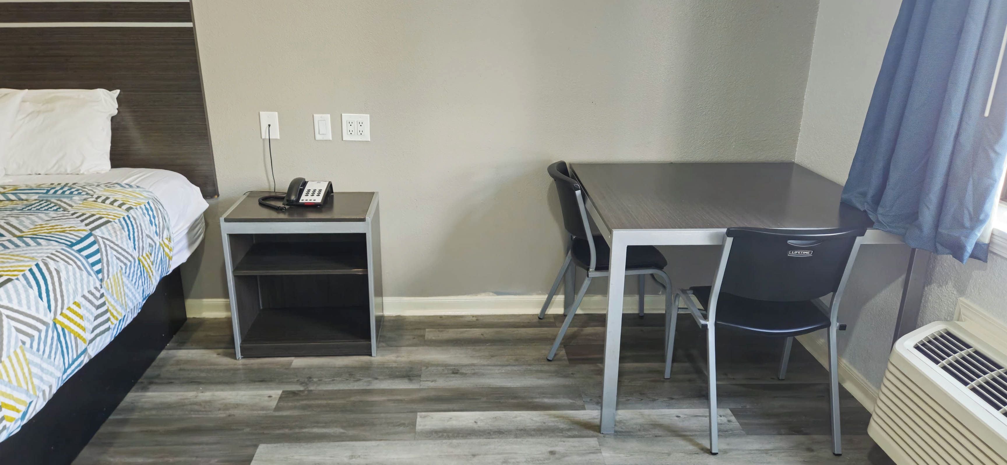 A hotel room with a bed, a desk, a chair, a telephone, and a heater.