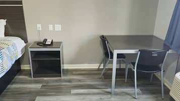 A hotel room with a bed, a desk, a chair, a telephone, and a heater.
