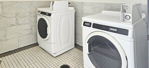 A laundry room with two white front-loading washing machines, a tiled floor, and a marble wall. - Motel 6 Houston, TX - Hwy 249 and Fallbrook (Houston)