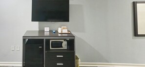 A room with a flat-screen TV mounted on the wall, a microwave, and a small table with a remote control and a tissue box.