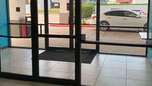 A view through a glass door into a parking lot with a white car parked. - Motel 6 Houston, TX - Hwy 249 and Fallbrook (Houston)