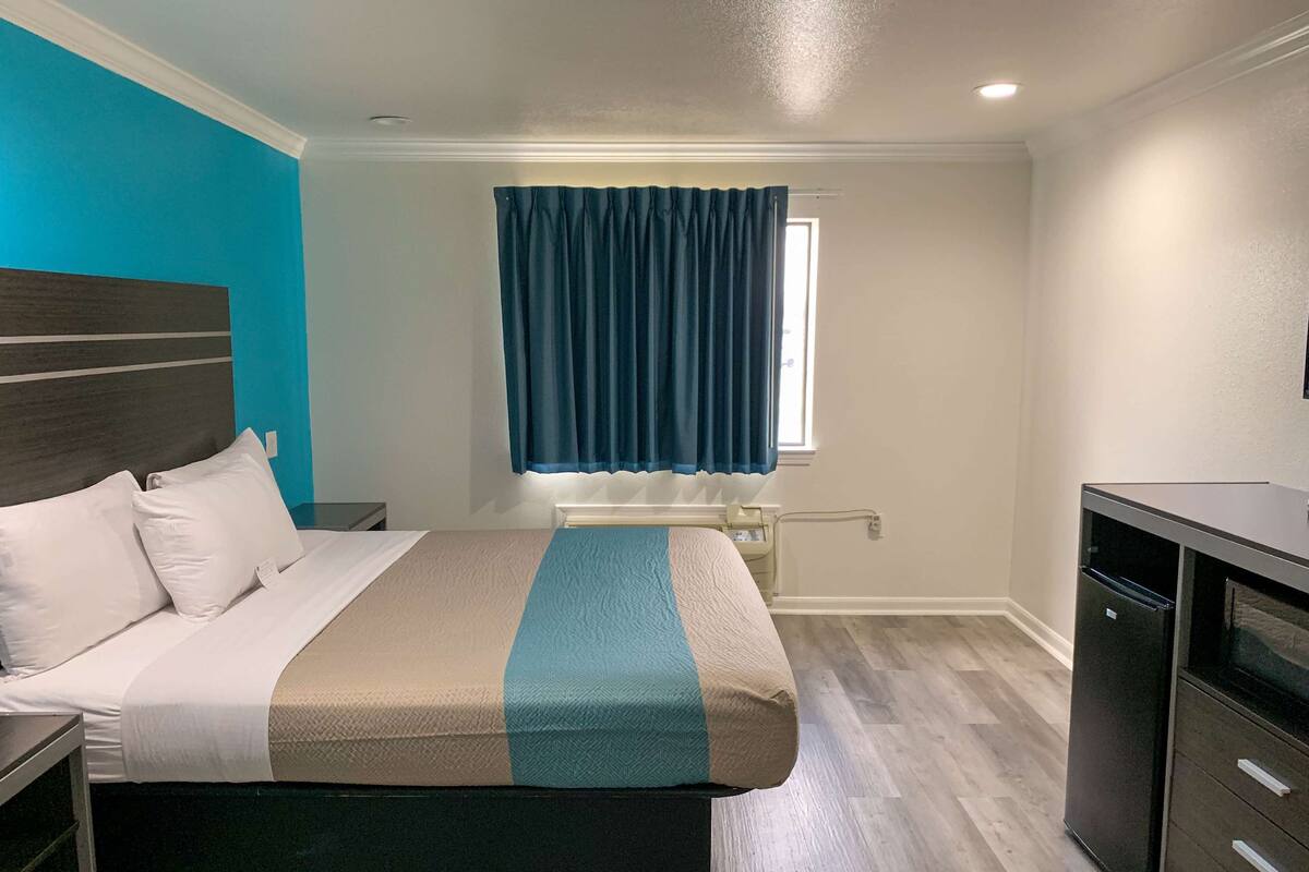 A hotel room with a bed, bedside table, a desk, a window with curtains, and a built-in wardrobe.