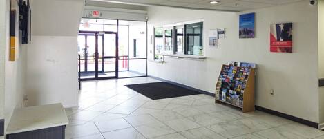 A clean, well-lit lobby with a reception desk, a glass door entrance, a window, and a book display.