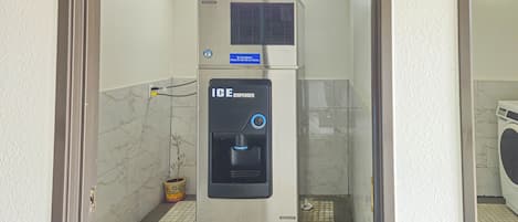 Un dispensador de hielo Hoshizaki en un baño con piso de baldosas y una lavadora al fondo.