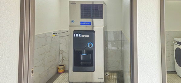 Un distributeur de glaçons Hoshizaki dans une salle de bain carrelée, avec une machine à laver en arrière-plan.