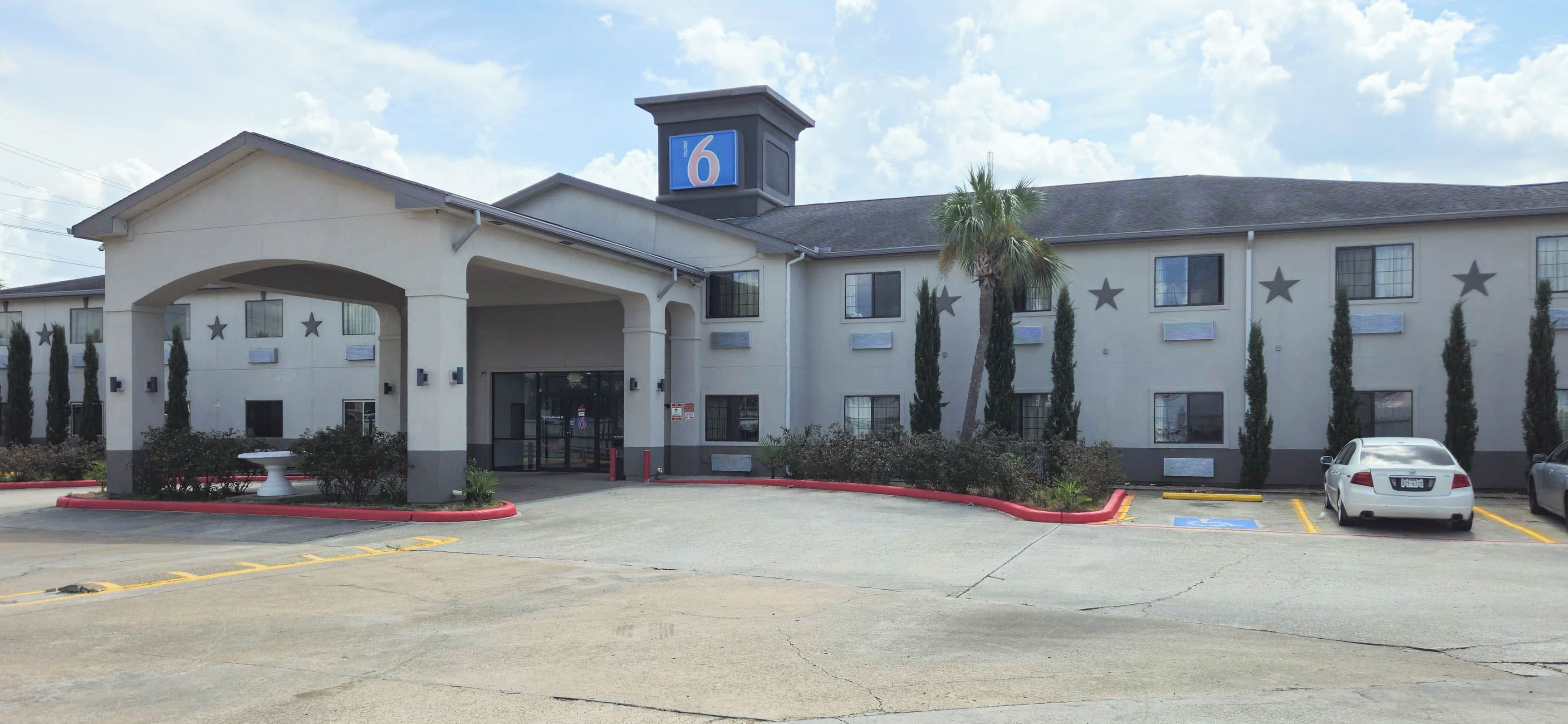 A hotel with a central entrance, multiple parking spaces, and a clear sky.