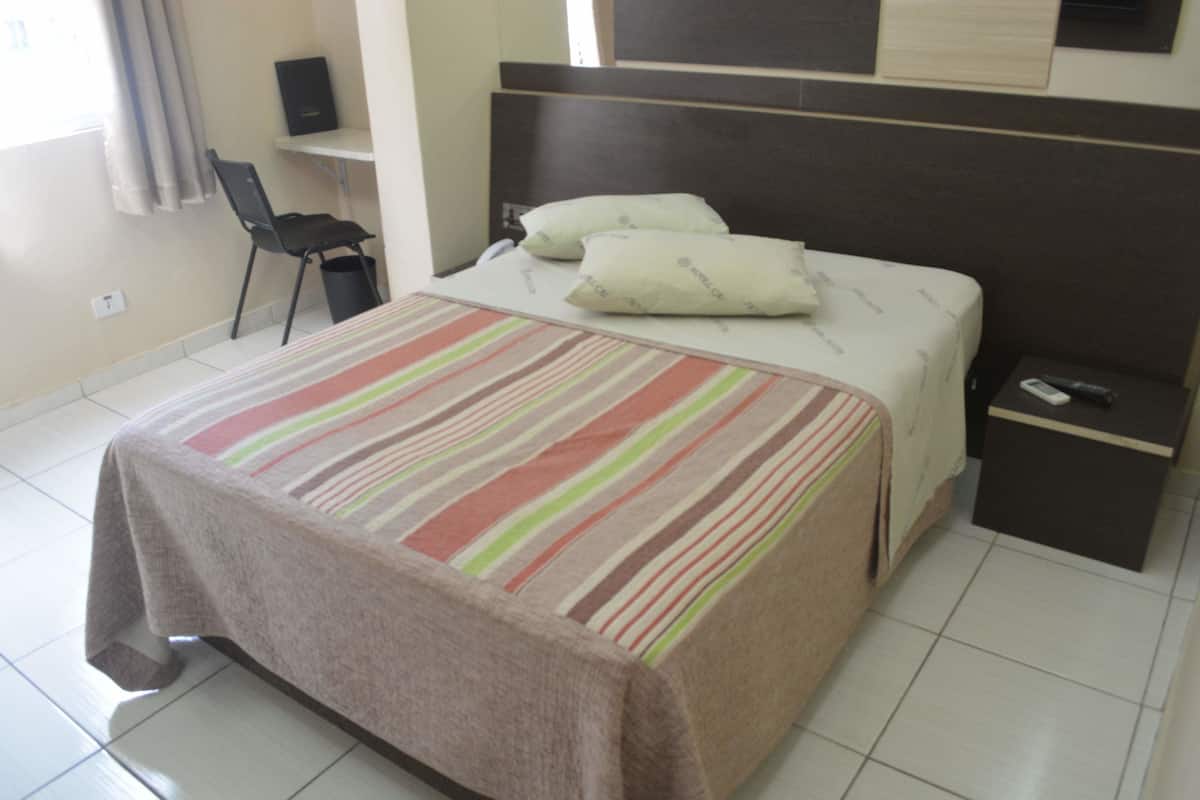 Ein Hotelzimmer mit Bett, Nachttisch, Sessel und Schreibtisch.