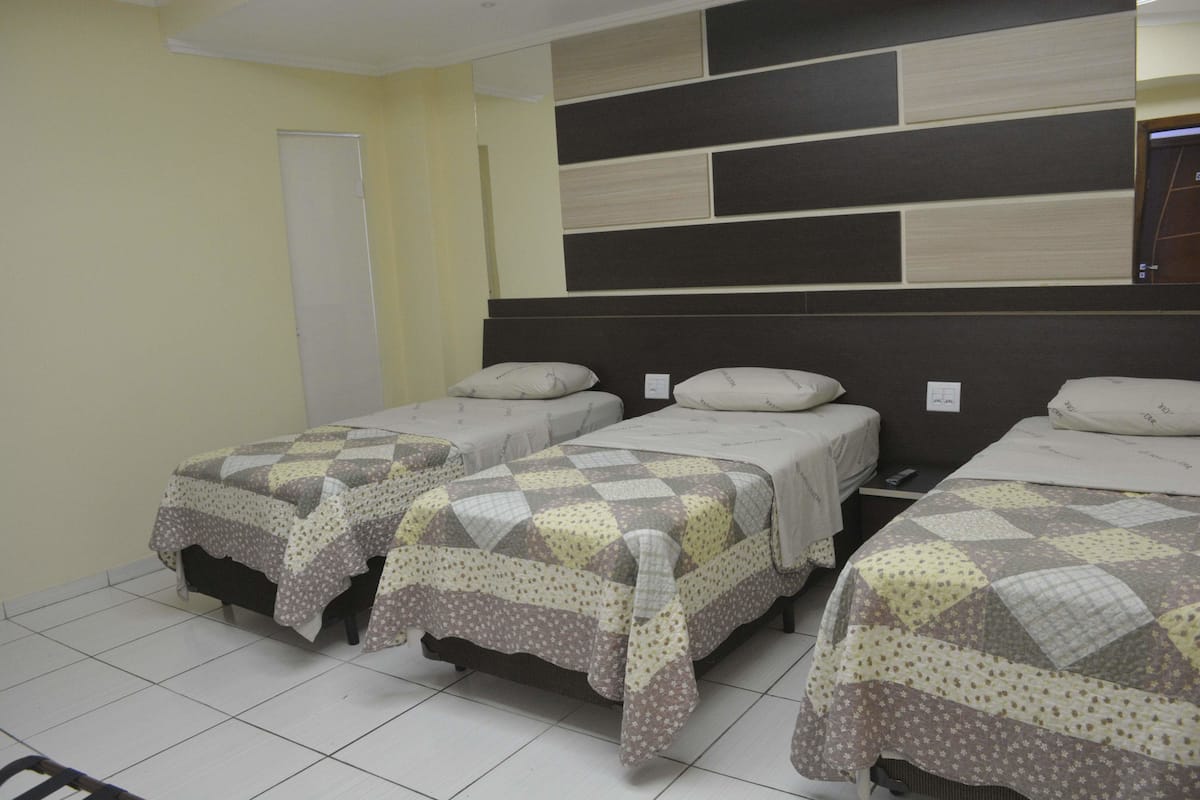 Ein Hotelzimmer mit drei Einzelbetten, jeweils mit gemusterten Bettdecken und Kissen. Das Zimmer verfügt über einen Fliesenboden und eine Wand mit modernem Design.