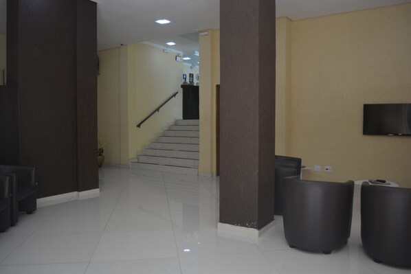 A clean, modern lobby with a staircase, a flat-screen TV mounted on the wall, and a reception desk. - Hotel Calstar (Sao Paulo)