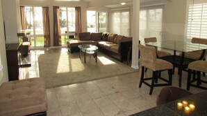 A spacious living room with a sectional sofa, a glass coffee table, and a dining area with a glass table and chairs. - 3 Bedroom Duplex with Ocean View (Newport Beach)