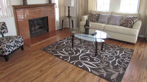 Una sala de estar con chimenea, una mesa de centro de vidrio, un sofá y un tapete estampado.