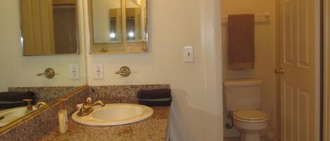 A bathroom with a granite countertop sink, a mirror, and a toilet.