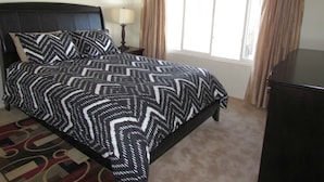 Un dormitorio con cama, mesita de noche, lámpara y ventana con cortinas.