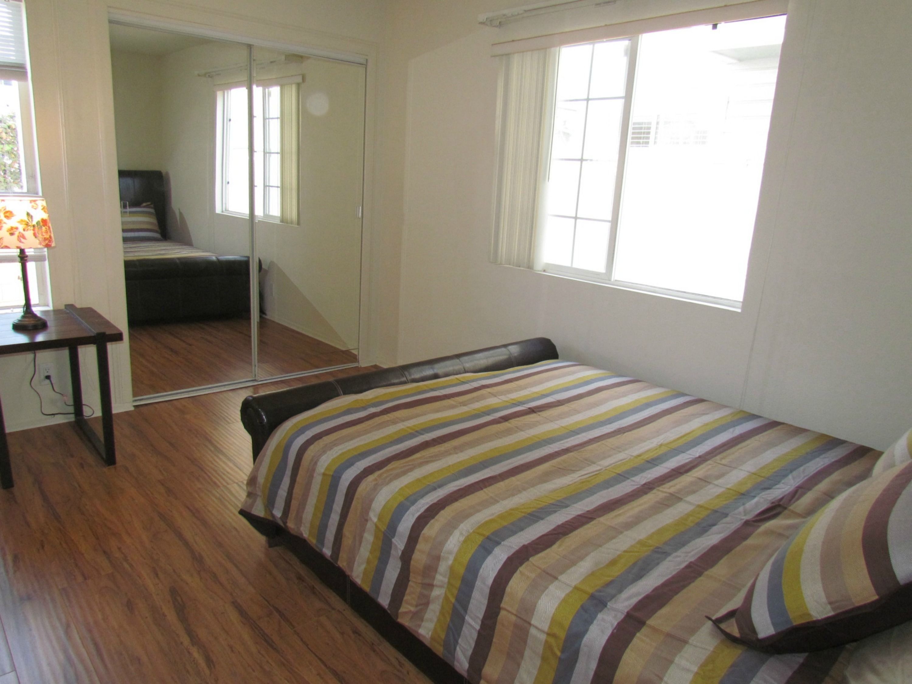 A bedroom with a bed, a mirror, a window, and a desk.