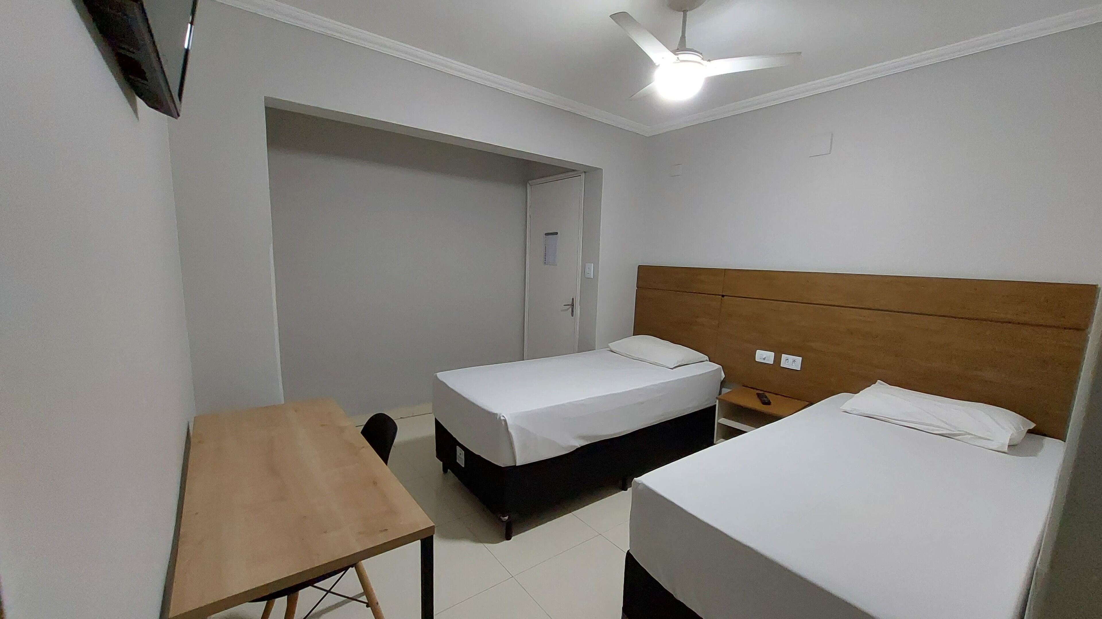 A hotel room with two single beds, a wooden table, a ceiling fan, and a door leading to a bathroom.