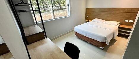 Une chambre à coucher de taille modeste, comprenant un lit, un bureau et une fenêtre donnant sur la verdure.