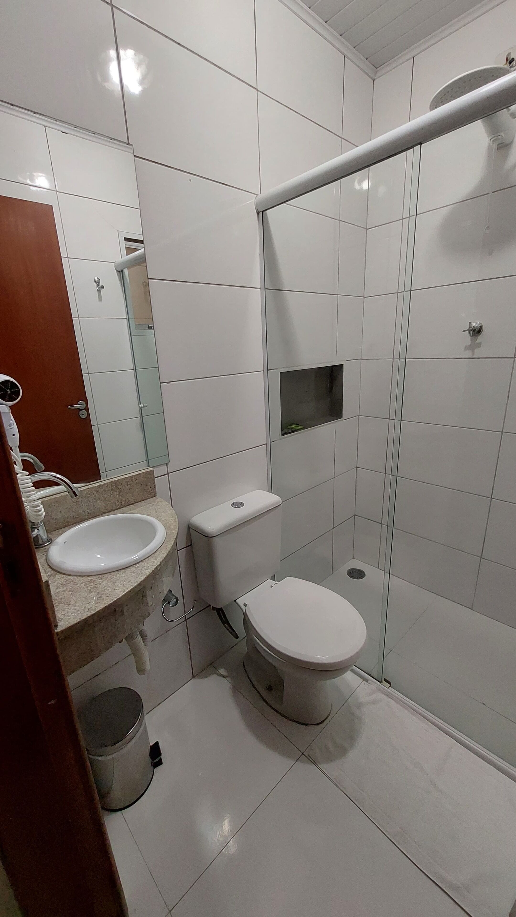 A modern bathroom with white tiles, a sink, toilet, and a glass shower enclosure.