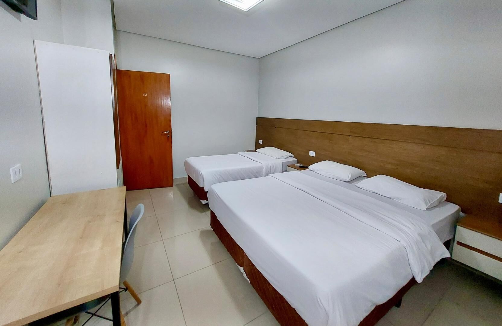 Une chambre d’hôtel avec trois lits simples, un bureau en bois et une chaise.