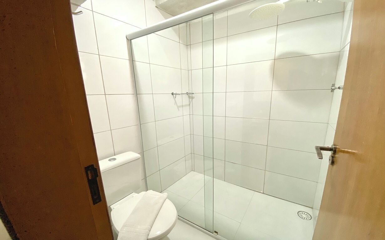 Un espacio de ducha pequeño y cerrado con puerta de cristal, un inodoro y un perchero para toallas.