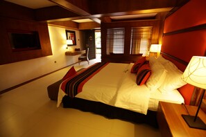A large bed with multiple pillows, a nightstand with a lamp, and a wooden headboard.