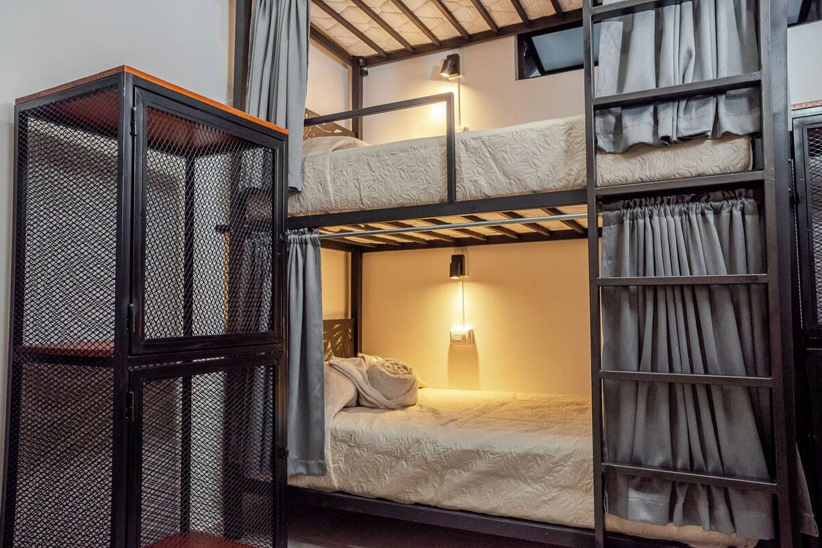 Une chambre avec un lit superposé, une échelle, une lampe suspendue et une étagère en treillis métallique.