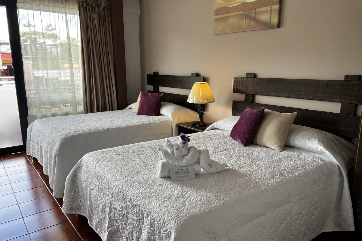 Une chambre d’hôtel avec deux lits, chacun recouvert d’une courtepointe blanche et doté d’une tête de lit. Une lampe se trouve sur la table de chevet entre les deux lits, et un tableau est accroché au mur au-dessus des lits.