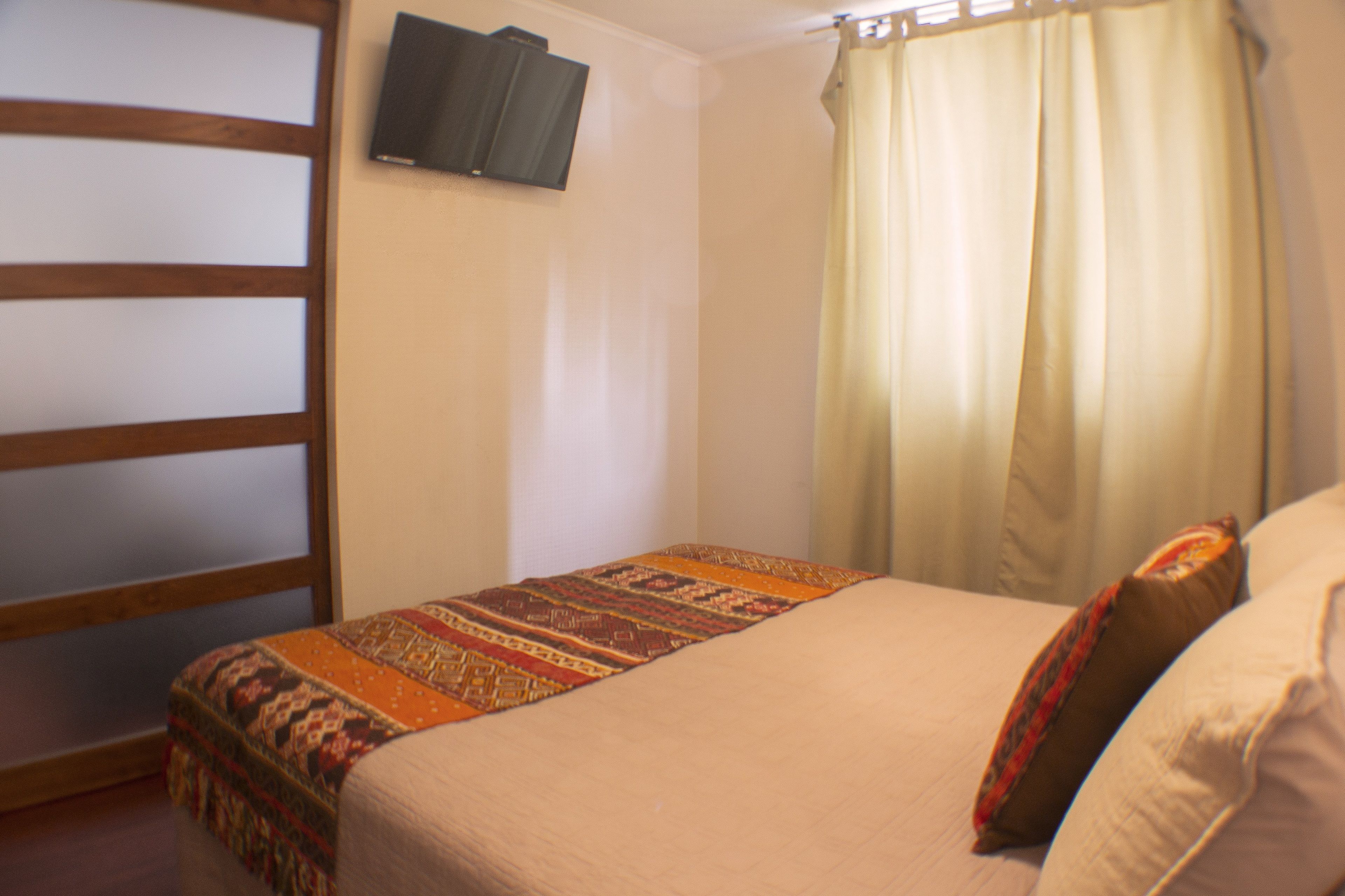 A bedroom with a bed, a television mounted on the wall, and a window with curtains.