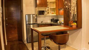 Cocina compacta con refrigerador, microondas y una pequeña zona de comedor con un taburete de bar.