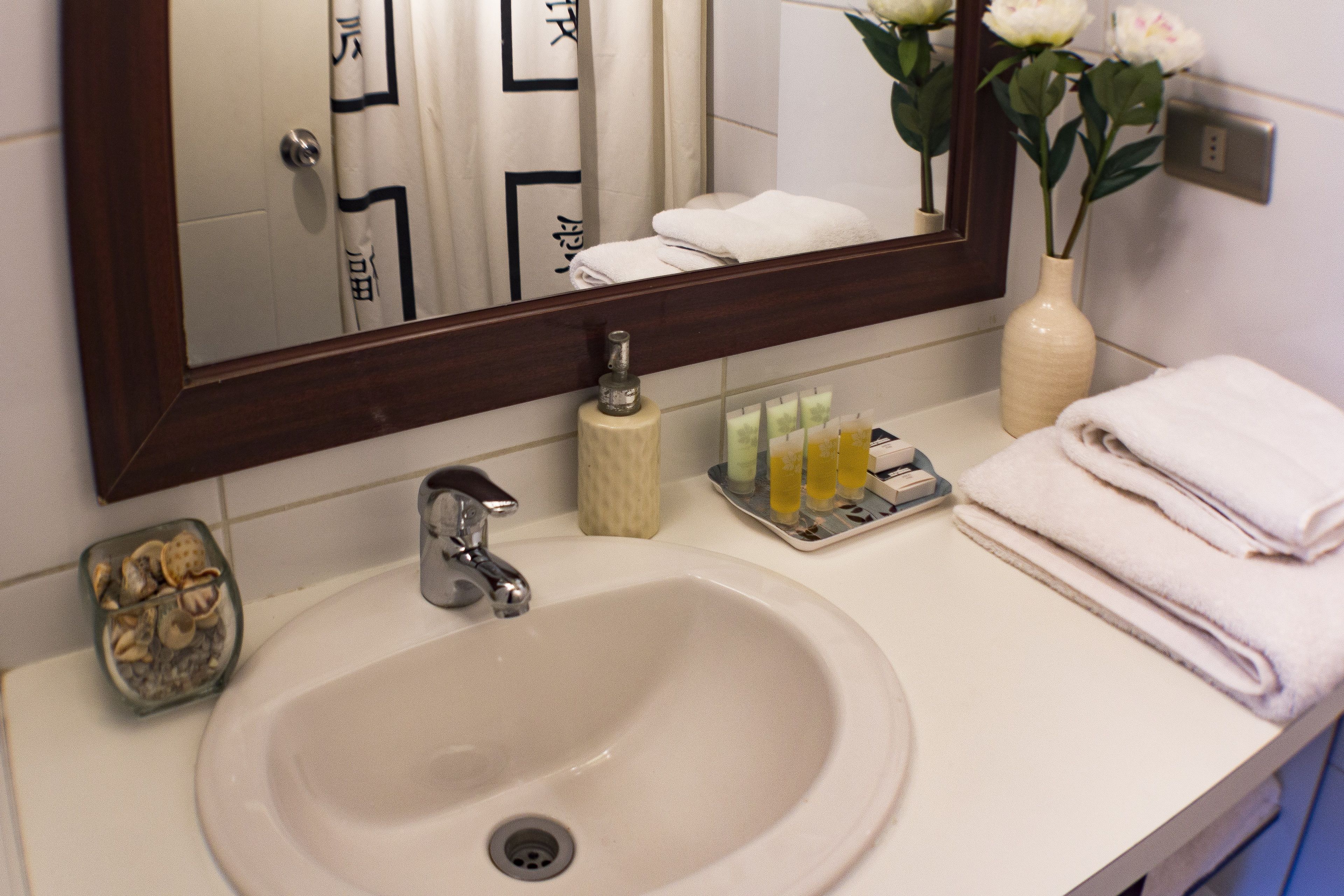 Un lavabo de salle de bain avec un miroir, un porte-serviettes, des articles de toilette et un vase avec des fleurs.