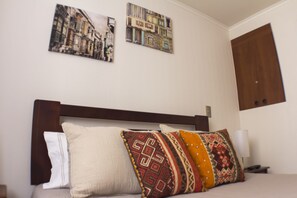 Una cama con cabecera de madera, varios almohadones y dos cuadros colgados en la pared.