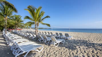 A beach with rows of white sun loungers and palm trees.