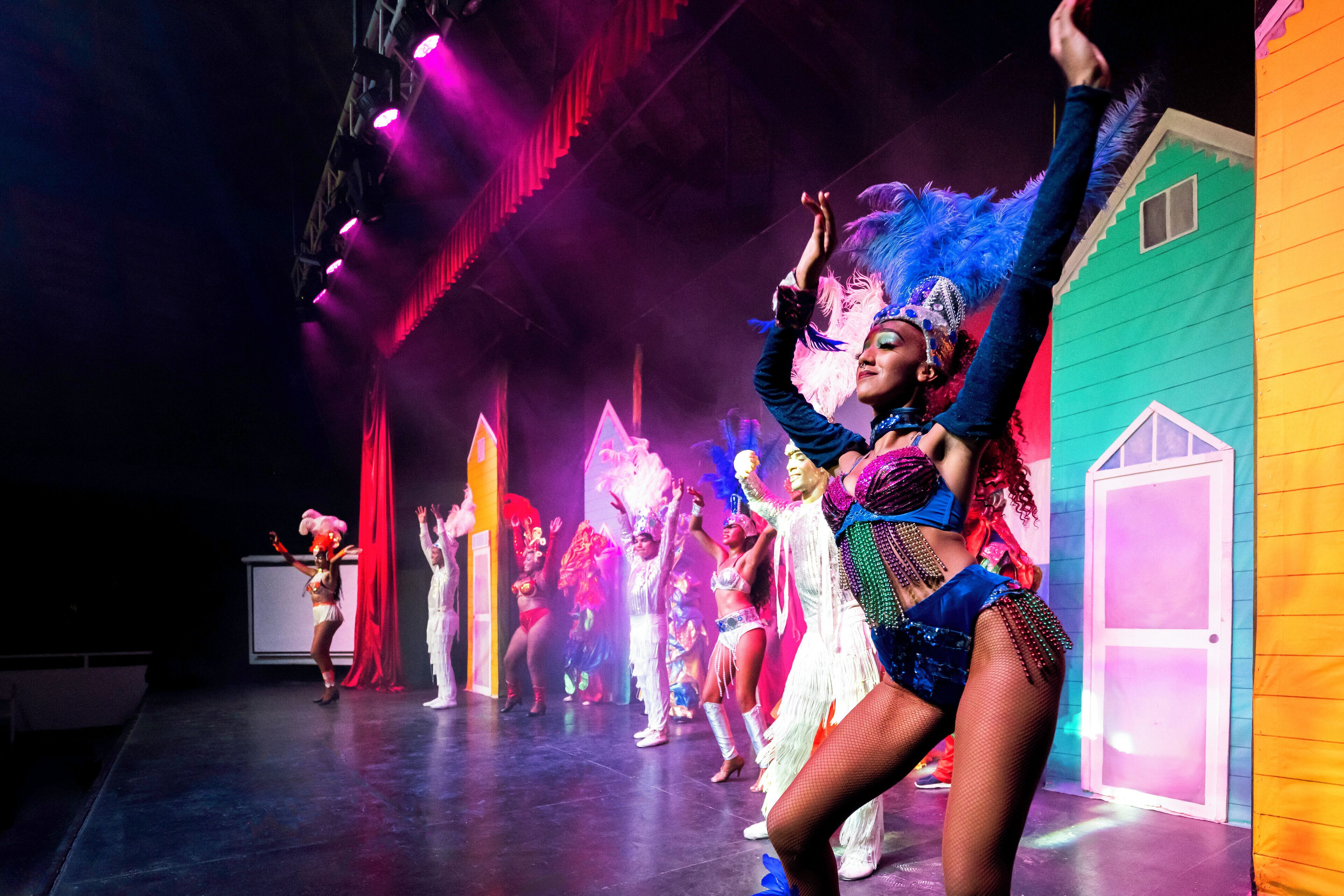 A stage with performers in colorful costumes, a green house-like structure, and a red curtain.