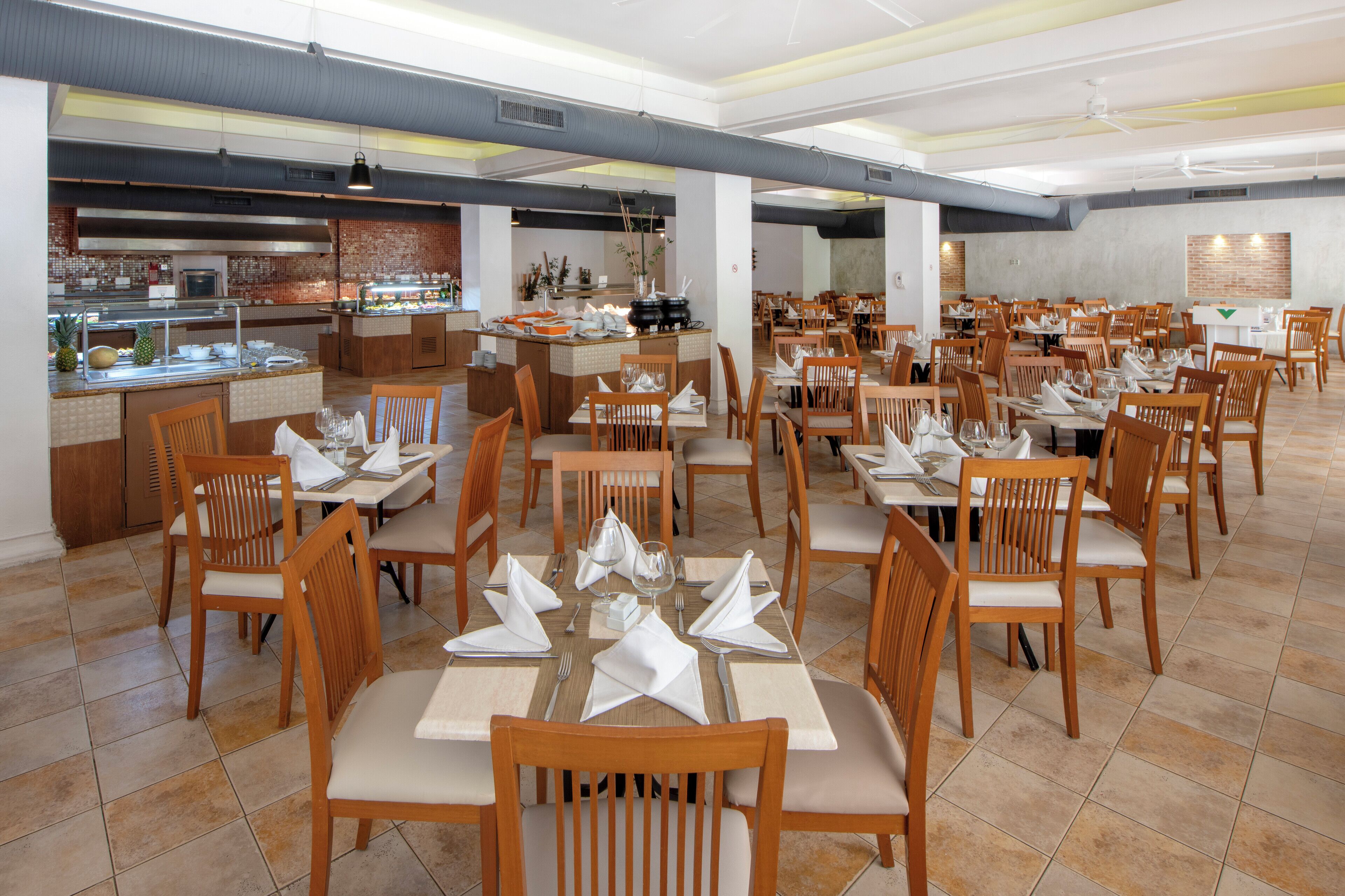 A spacious dining area with multiple tables and chairs, a buffet counter, and a kitchen area.