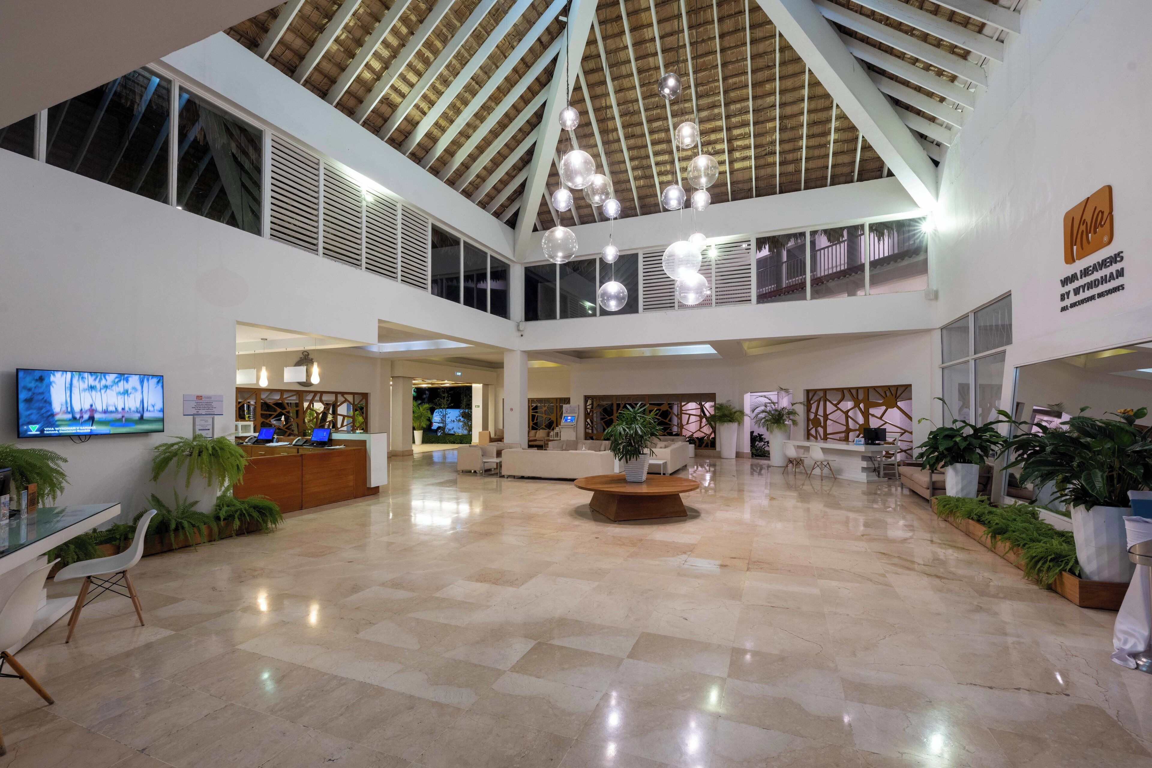 Een ruime lobby met een hoge plafond, een receptiebalie, zithoeken en potplanten.
